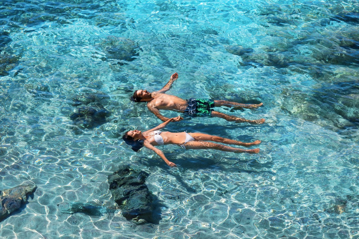 Torquise waters Two people floating on clear blue water with rocks visible below.