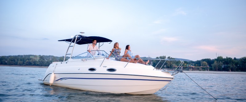 Friends on a boat enjoying Boat with three people on a calm river, trees in the background.