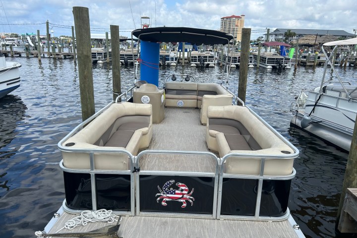 Docked pontoon boat with cushioned seating and canopy under a cloudy sky.