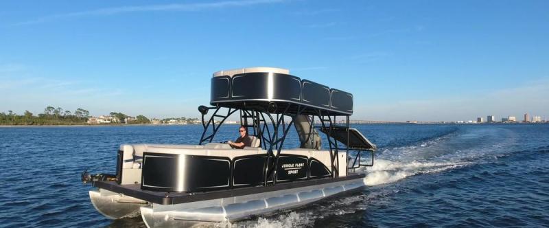 Black pontoon boat with upper deck cruising on a lake.